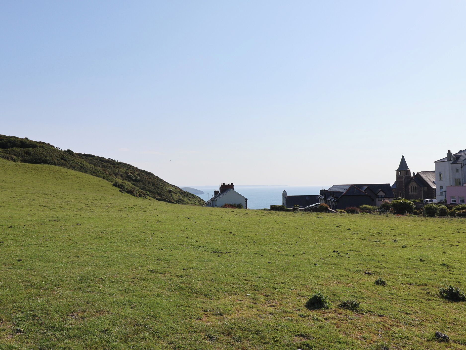 Een kustlandschap met een grasveld, een kerk en woongebouwen.