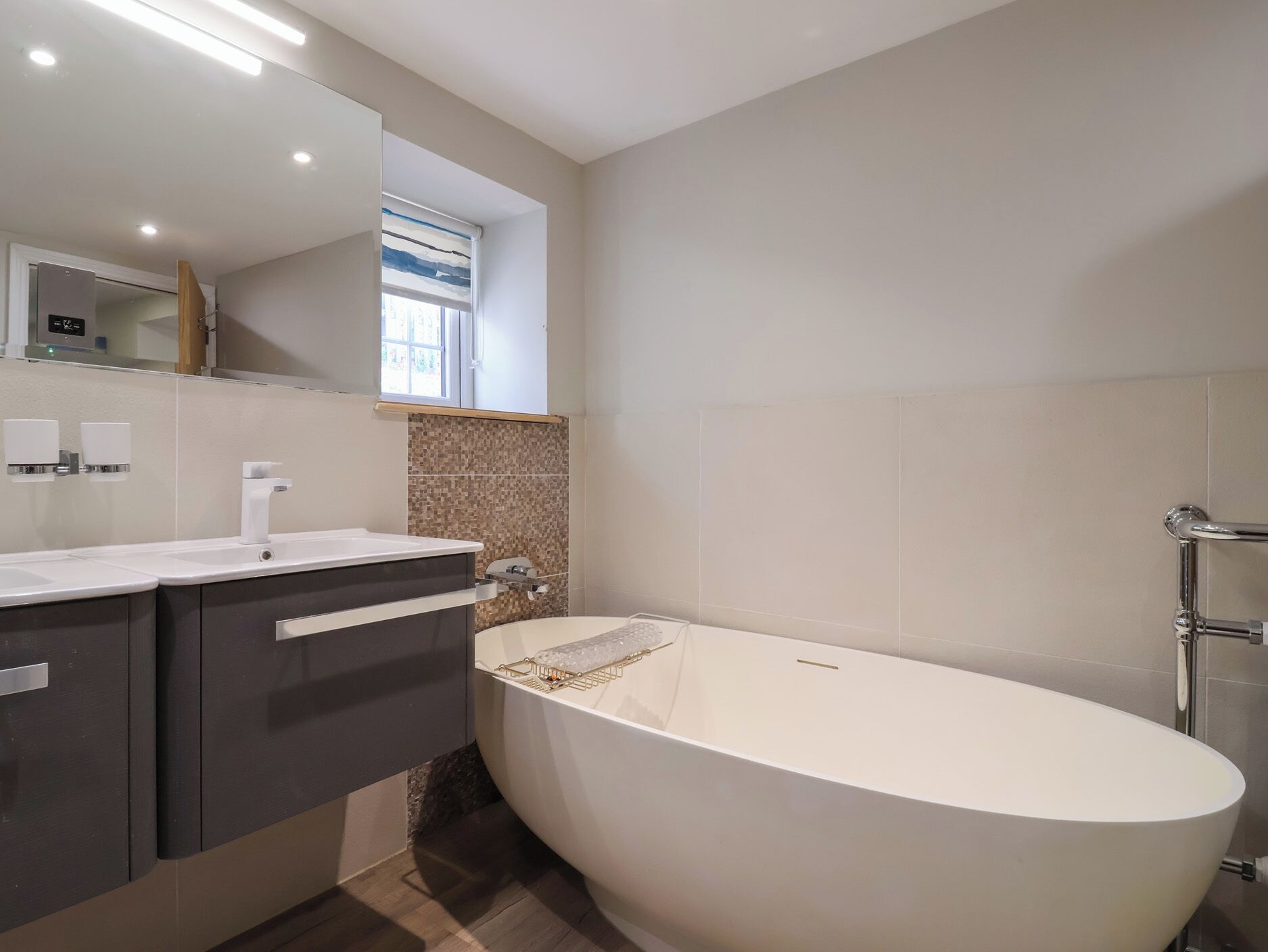 A modern bathroom with a freestanding bathtub, a vanity with a mirror, and a window above the sink.