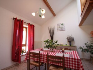 Un coin repas avec une nappe à carreaux, des chaises en bois, un luminaire suspendu et une fenêtre ornée de rideaux rouges.