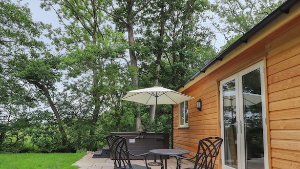 Un patio con una mesa, sillas, una sombrilla y un edificio de madera con puertas de cristal.