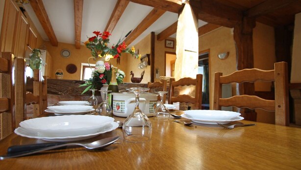 A wooden dining table set with plates, cutlery, and a vase of flowers. - Charming Nature Retreat: Cozy Cottage with Fireplace and Scenic Views (Girmont-Val-d'Ajol)