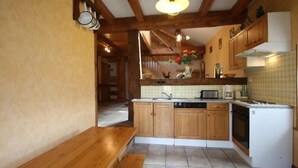 A kitchen with wooden cabinets, a built-in oven, and a bench. - Charming Nature Retreat: Cozy Cottage with Fireplace and Scenic Views (Girmont-Val-d'Ajol)