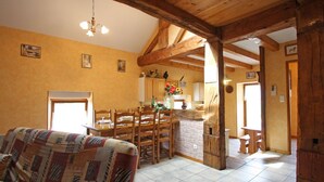 A cozy, rustic interior with exposed wooden beams, a dining area with a wooden table and chairs, a kitchen with a stone wall, and a patterned sofa. - Charming Nature Retreat: Cozy Cottage with Fireplace and Scenic Views (Girmont-Val-d'Ajol)