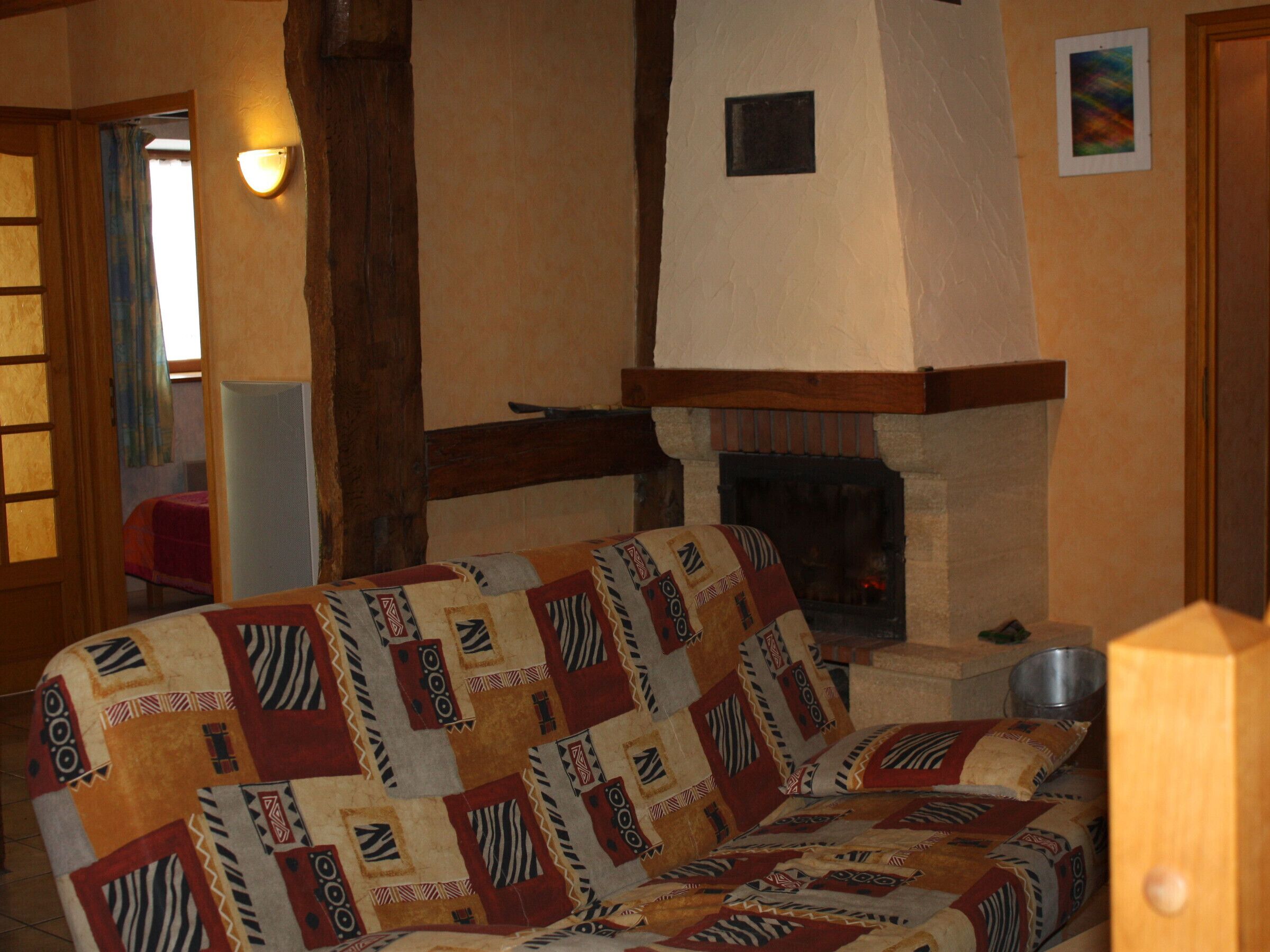 A cozy living room with a fireplace, a patterned sofa, and a wooden ceiling beam.