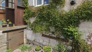 A stone building with a wooden door and windows, covered in ivy. There are potted plants on the ground. - Athelstan Cottage (Stroud)