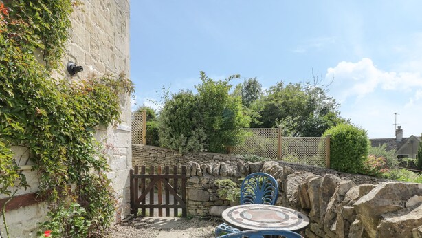 A courtyard with stone walls, a wooden gate, and outdoor seating with blue chairs. - Athelstan Cottage (Stroud)