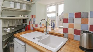 A kitchen with a white sink, wooden countertop, and a window with a view. - Athelstan Cottage (Stroud)