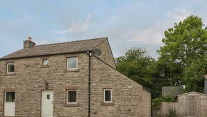 A stone building with a sloped roof, a white door, and multiple windows. - Limers Cottage (Buxton)