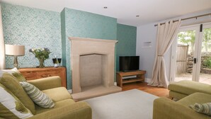 A living room with a fireplace, a television on a wooden stand, and two green armchairs. - Limers Cottage (Buxton)