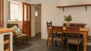 A dining area with a wooden table and chairs, a vase with flowers, and a wooden shelf above the table. - Limers Cottage (Buxton)