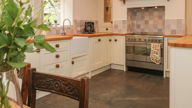 A kitchen with white cabinets, a stainless steel oven, and a wooden countertop. - Limers Cottage (Buxton)