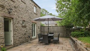 A stone building with a patio featuring a table and chairs under a large umbrella. - Limers Cottage (Buxton)