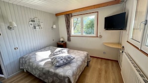 A bedroom with a bed, a TV, a window, and a radiator. - Cozy Mountain Retreat Near Gérardmer – Ski, Hike, Relax! (Gérardmer)