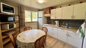 A compact kitchen with a dining table, chairs, a microwave, a stove, and cabinets. - Cozy Mountain Retreat Near Gérardmer – Ski, Hike, Relax! (Gérardmer)