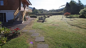 A wooden house with a staircase leading to a deck, surrounded by a well-maintained lawn and garden. - Cozy Mountain Retreat Near Gérardmer – Ski, Hike, Relax! (Gérardmer)