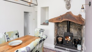 A dining area with a wooden table and chairs, a fireplace with a log basket, and a deer head mounted on the wall. - Bryn Peris (Moelfre)