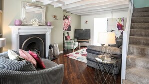 A living room with a fireplace, a television, and a staircase. - Bryn Peris (Moelfre)