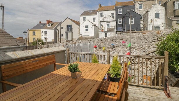 Eine Holzterrasse mit Tisch und Stühlen, mit Blick auf eine Steinsäule und bunte Flaggen.