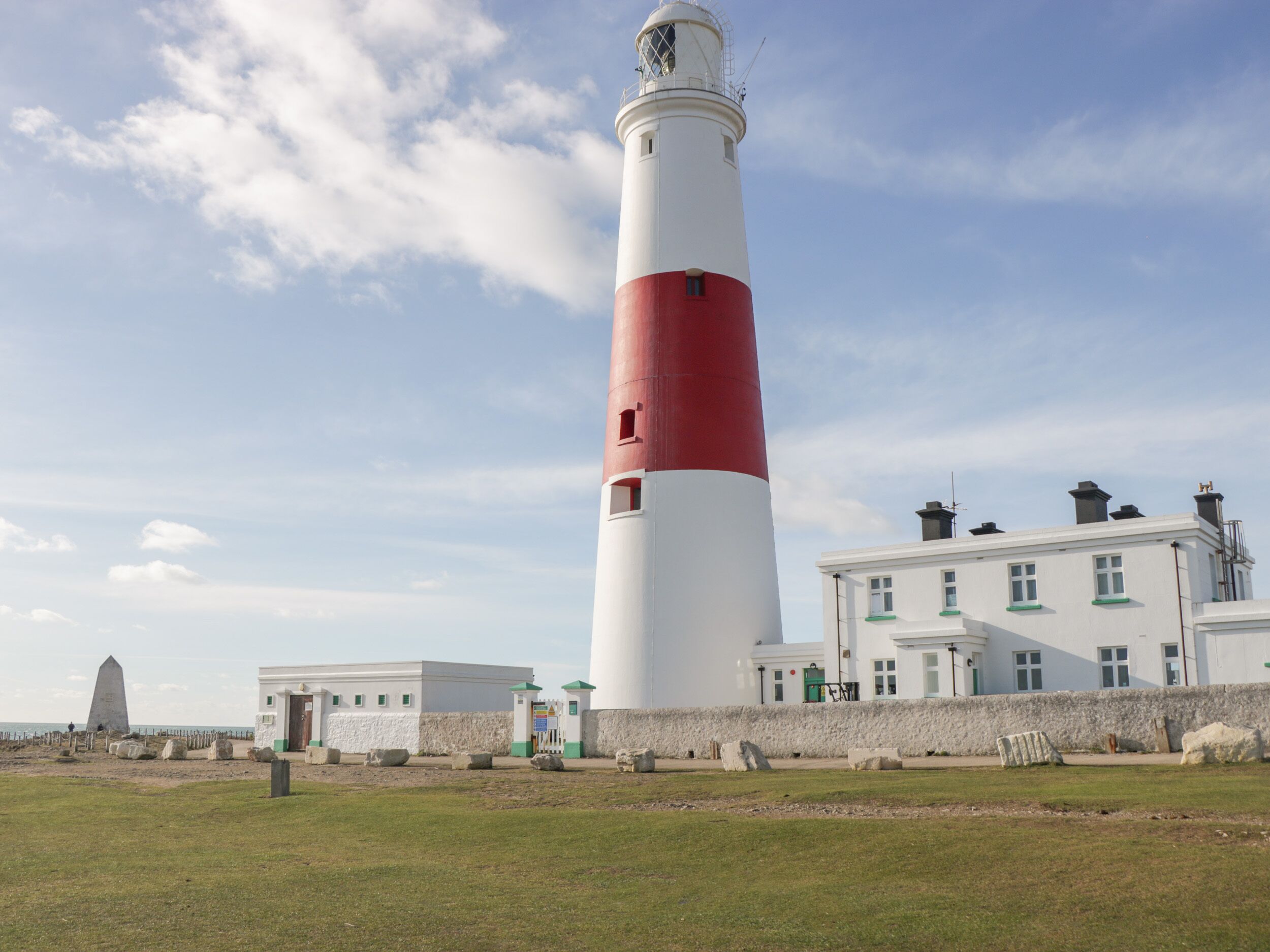 A lighthouse with a white and red color scheme, a white building with green trim, and a grassy area in front.