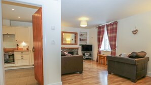 A living room with a fireplace, a television, and a dining area with a table and chairs. - Holly Tree Cottage (Coniston)