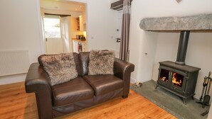 Una sala de estar acogedora con un sofá de cuero, una chimenea de piedra y una cocina visible a través de una puerta abierta.