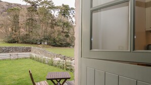 Un patio con una mesa y sillas de piedra, un muro de piedra, y vista a un área verde con árboles y un muro de piedra al fondo.