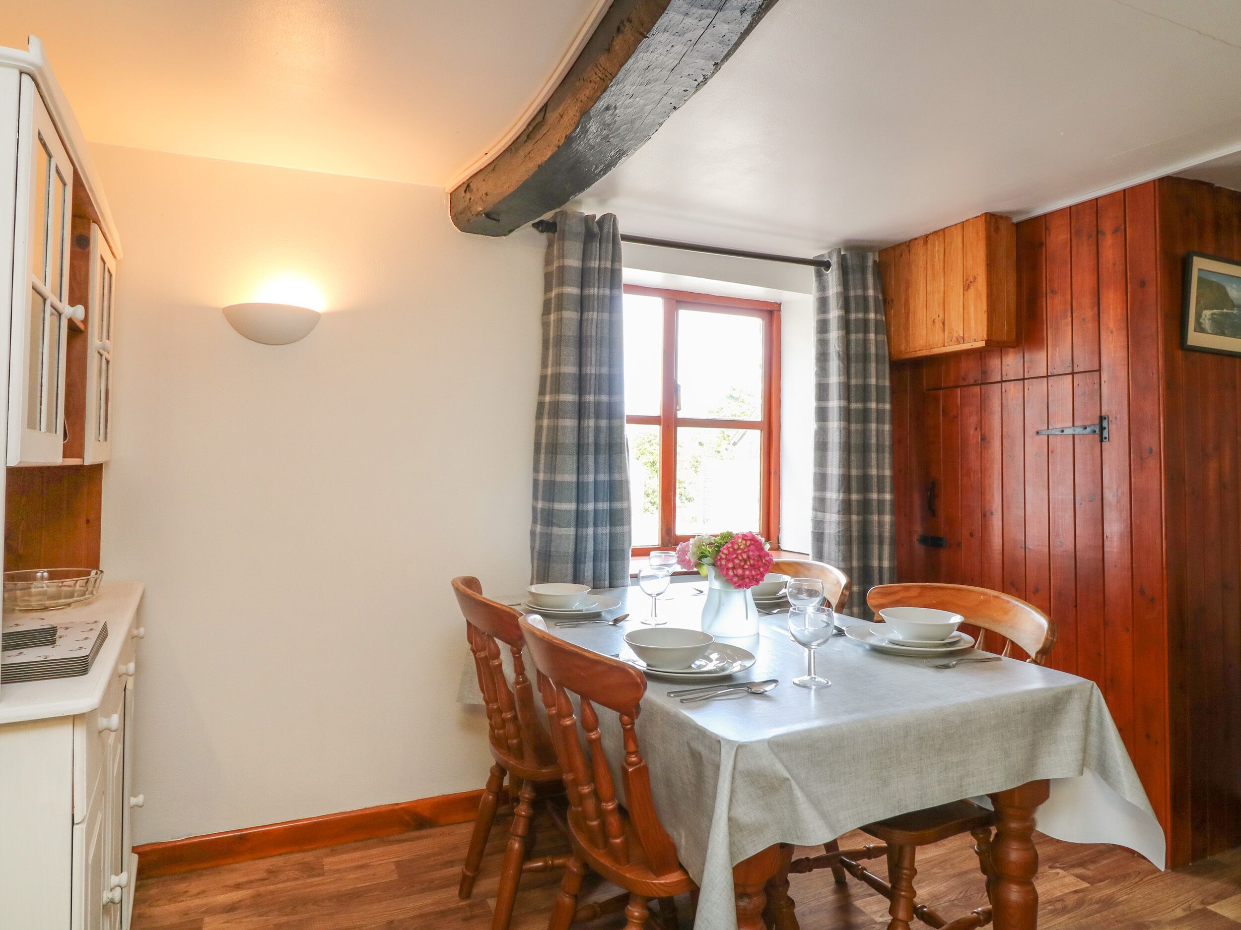 Ein Essbereich mit einem Tisch für vier Personen, Holzsesseln, einem weißen Schrank und einem Fenster mit Vorhängen.