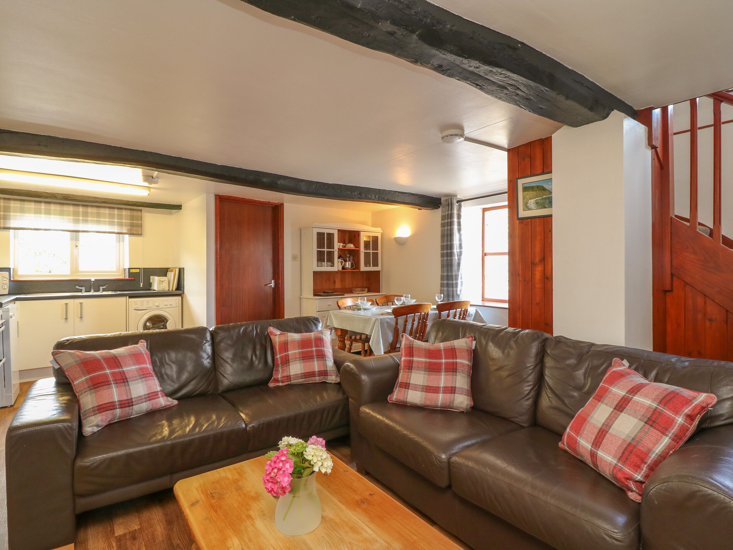 A cozy living room with a brown leather sofa, a wooden coffee table, and a dining area with a table and chairs.