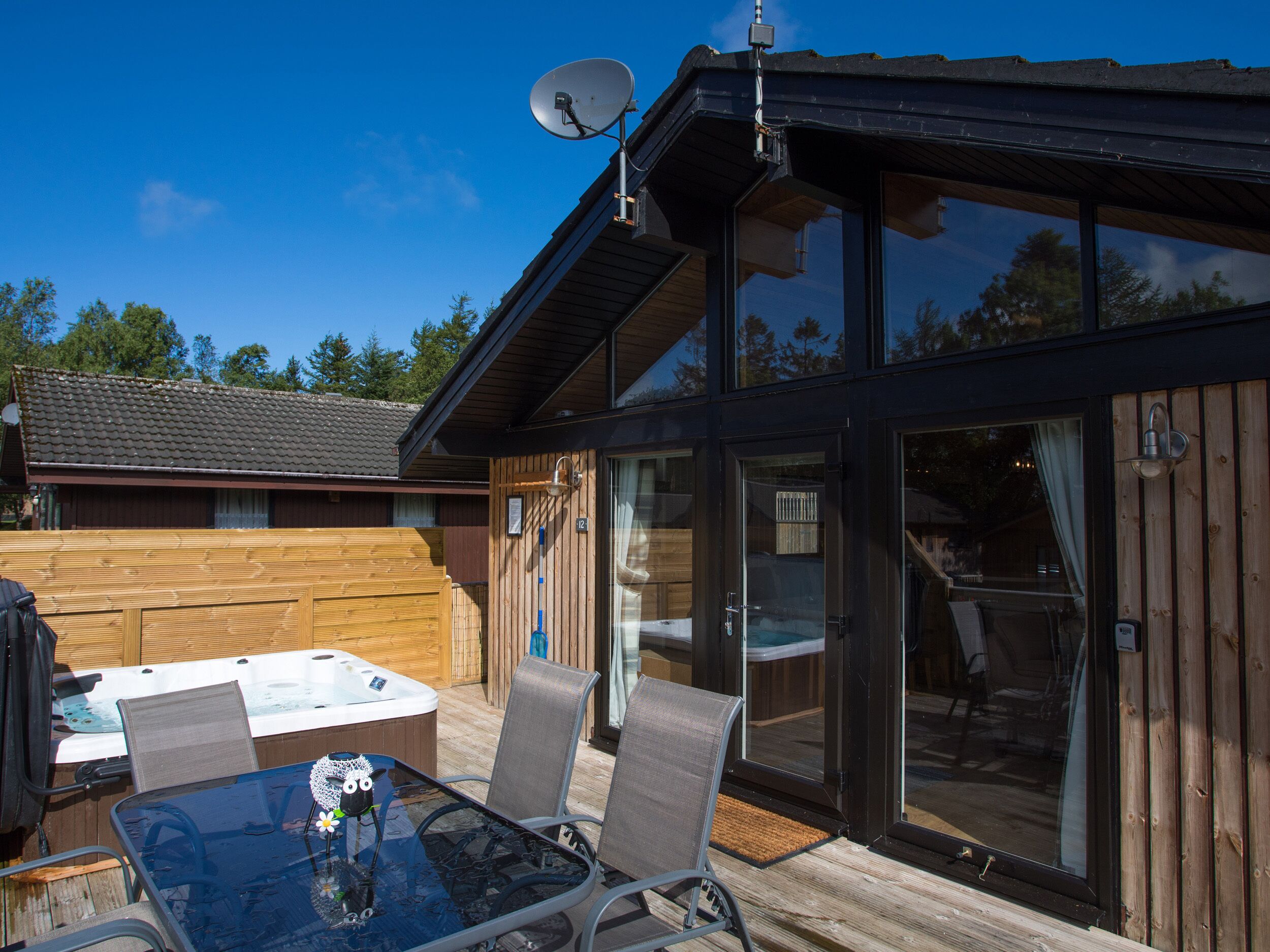 Een moderne buitenruimte met een glazen tafel, metalen stoelen en een jacuzzi.