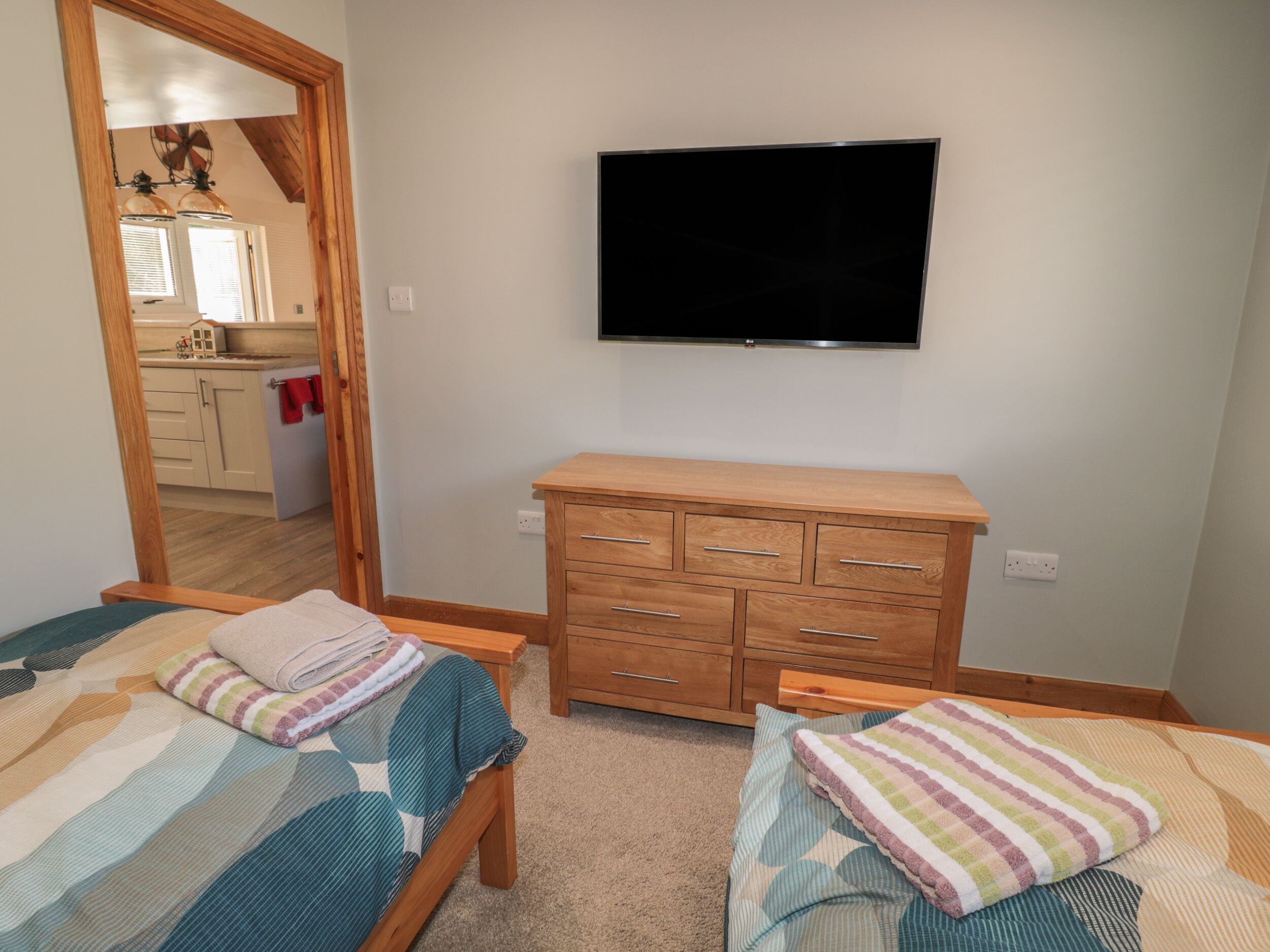 Ein Schlafzimmer mit zwei Betten, einer Holzkommode und einem an der Wand befestigten Fernseher.