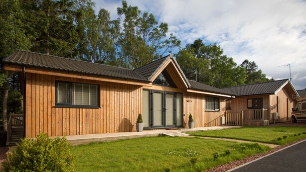 A row of wooden cabins with a grassy lawn and a paved driveway. - Treetops (Newcastle-upon-Tyne)