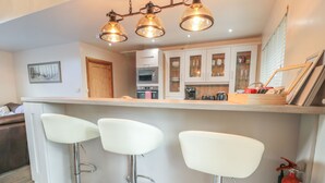 A modern kitchen with a central island, bar stools, and a fire extinguisher. - Treetops (Newcastle-upon-Tyne)