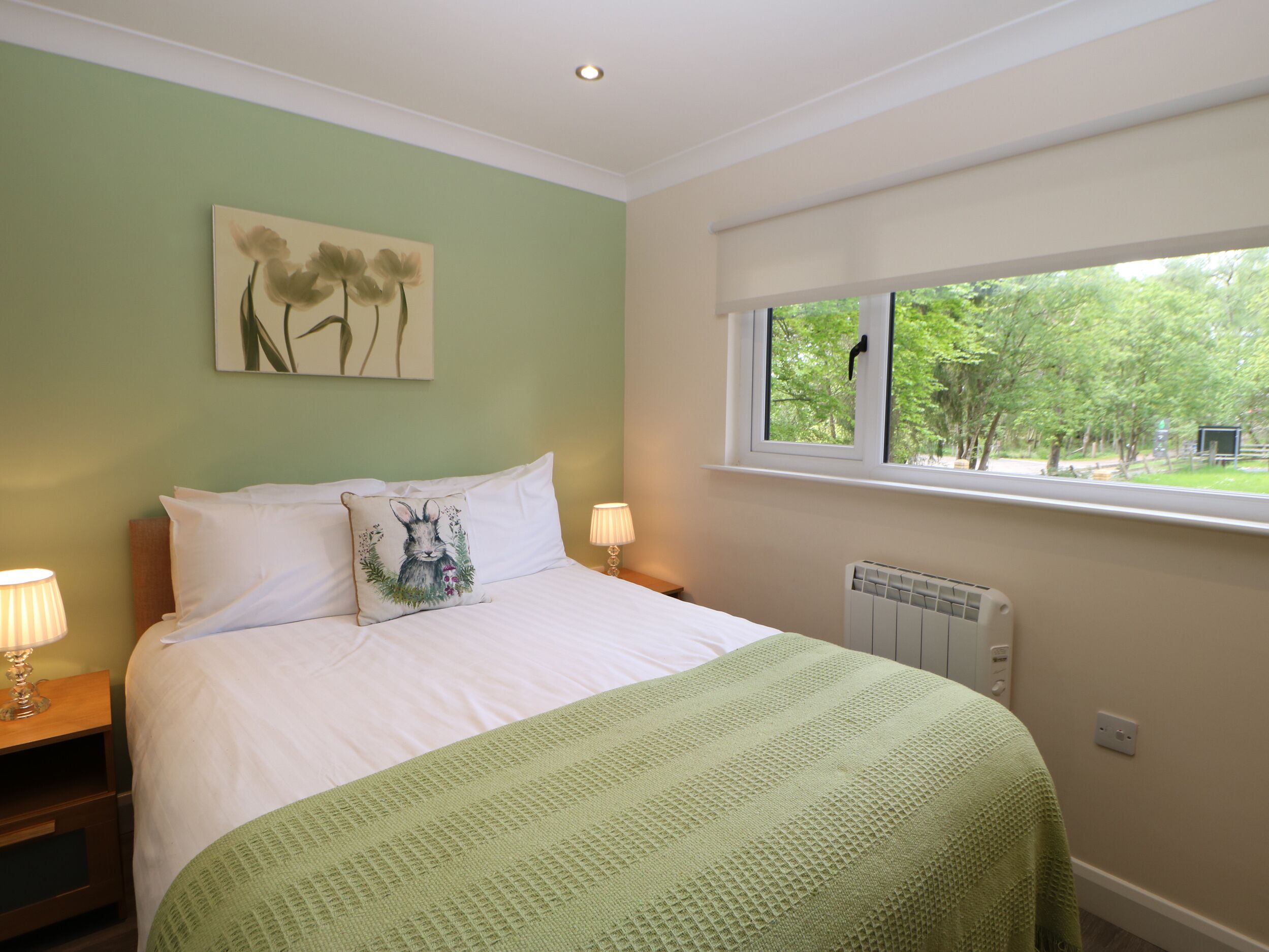 A bedroom with a bed, a window with a view of trees, a radiator, and a wall with a painting.