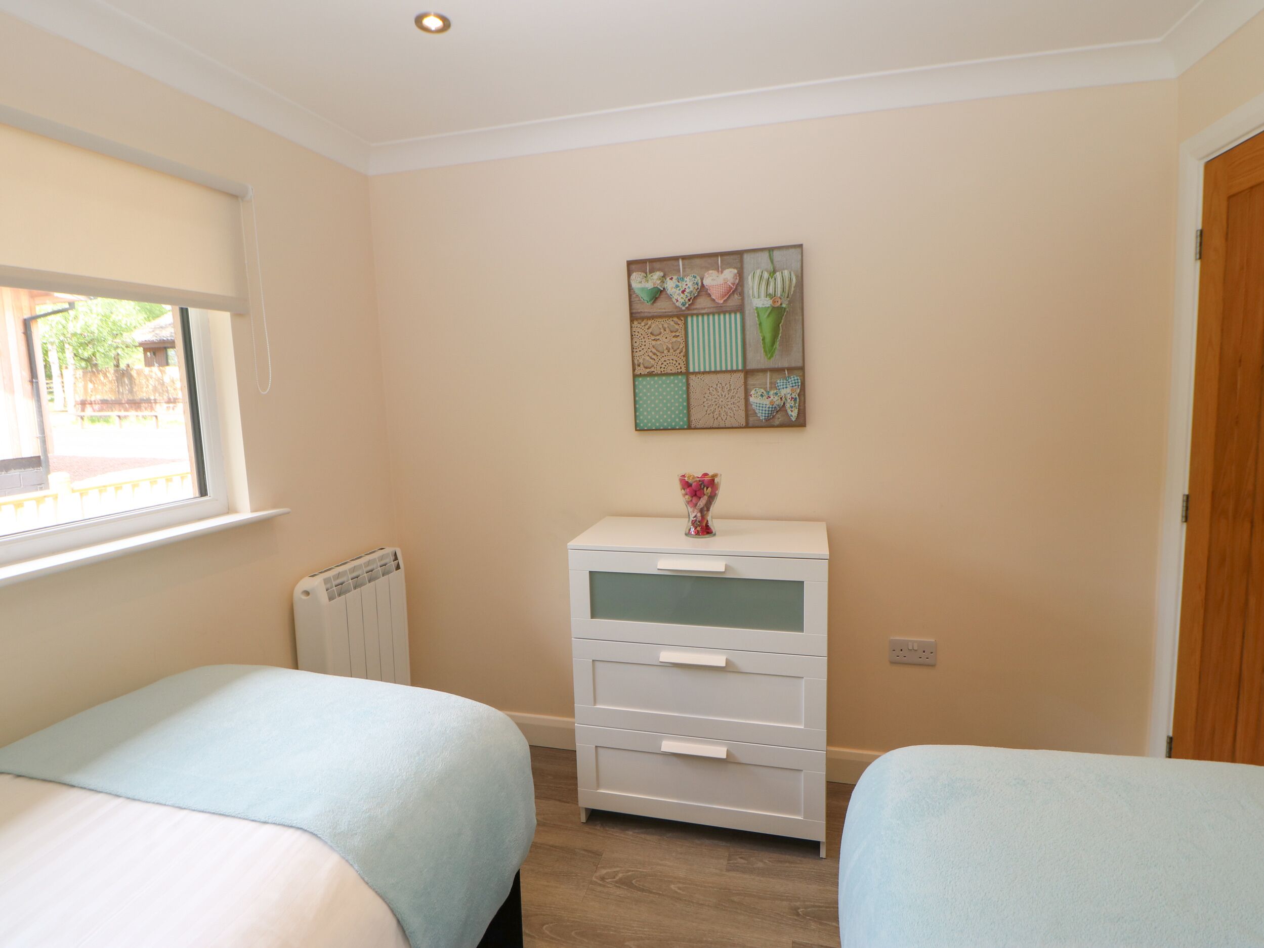 A bedroom with two beds, a dresser, a radiator, and a wall decoration.