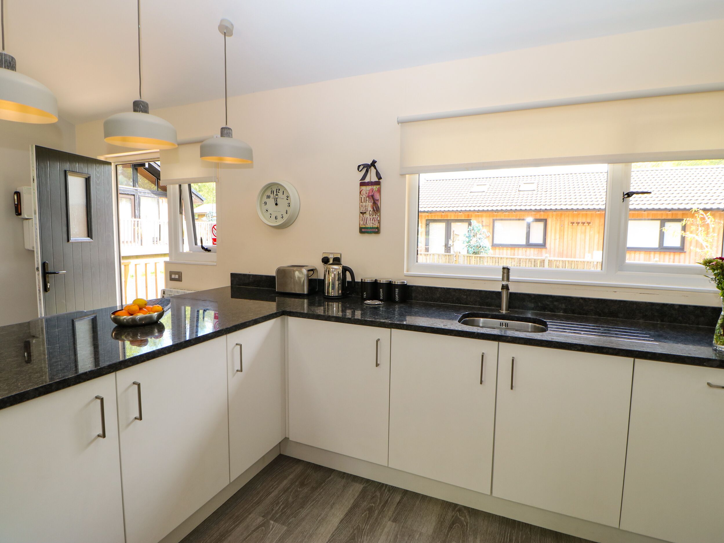 A modern kitchen with white cabinets, a black countertop, a stainless steel sink, and pendant lighting.
