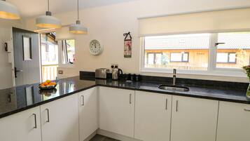 A modern kitchen with white cabinets, a black countertop, a stainless steel sink, and pendant lighting.