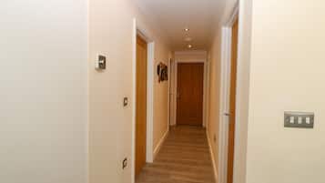 A narrow hallway with wooden flooring, white walls, and a wooden door at the end.