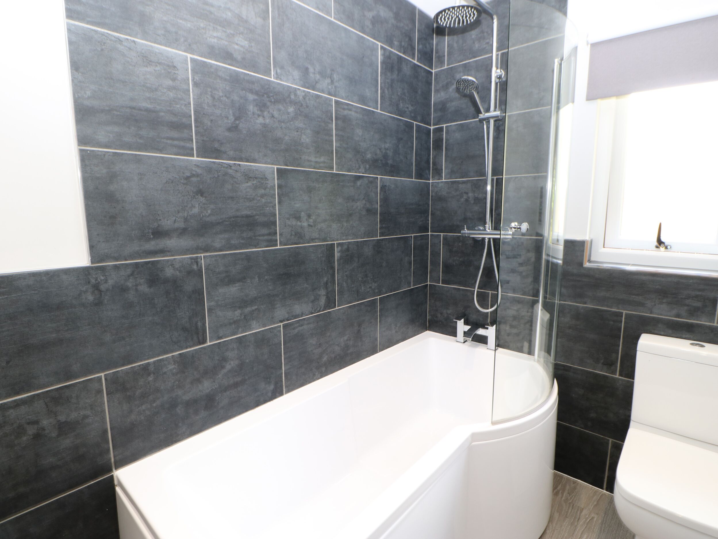 A modern bathroom with dark tiled walls, a white bathtub, and a shower.