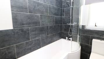 A modern bathroom with dark tiled walls, a white bathtub, and a shower.