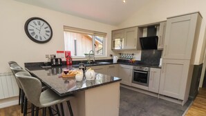 A modern kitchen with a central island, bar stools, a microwave, oven, and a clock on the wall. - Barn Owl (Newcastle-upon-Tyne)