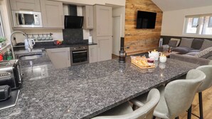 A modern kitchen with granite countertops, stainless steel appliances, and a wooden accent wall. - Barn Owl (Newcastle-upon-Tyne)