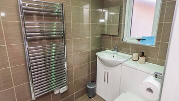 Et badeværelse med et kromhåndklædetørrestativ, en vask, et spejl og et toilet.