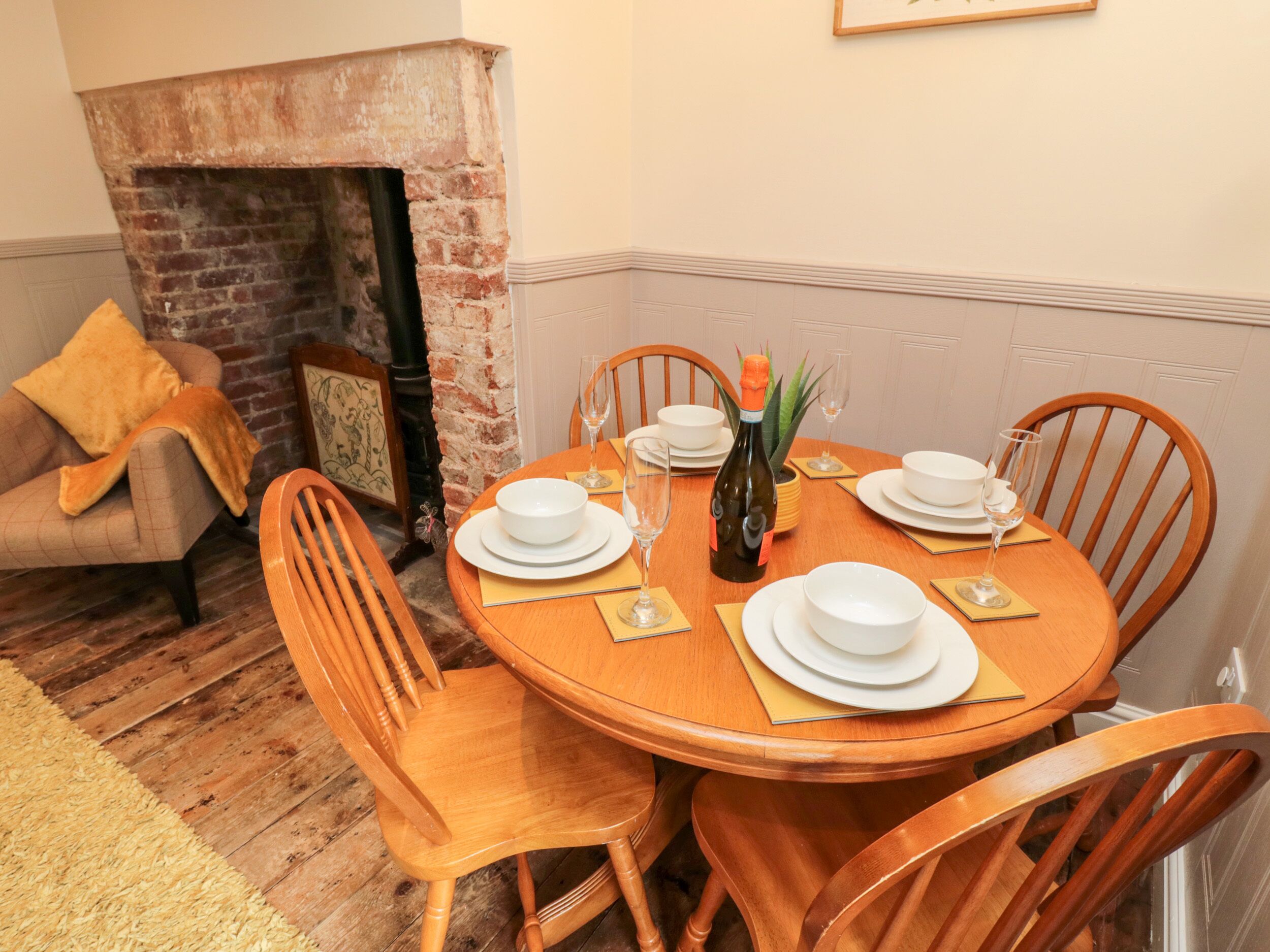 A dining area with a brick fireplace, wooden dining table, chairs, and a sofa with a throw blanket.