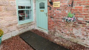 Un edificio de ladrillo con una puerta verde, una ventana con flores y un letrero que dice "BRIDGEND BOTHY".