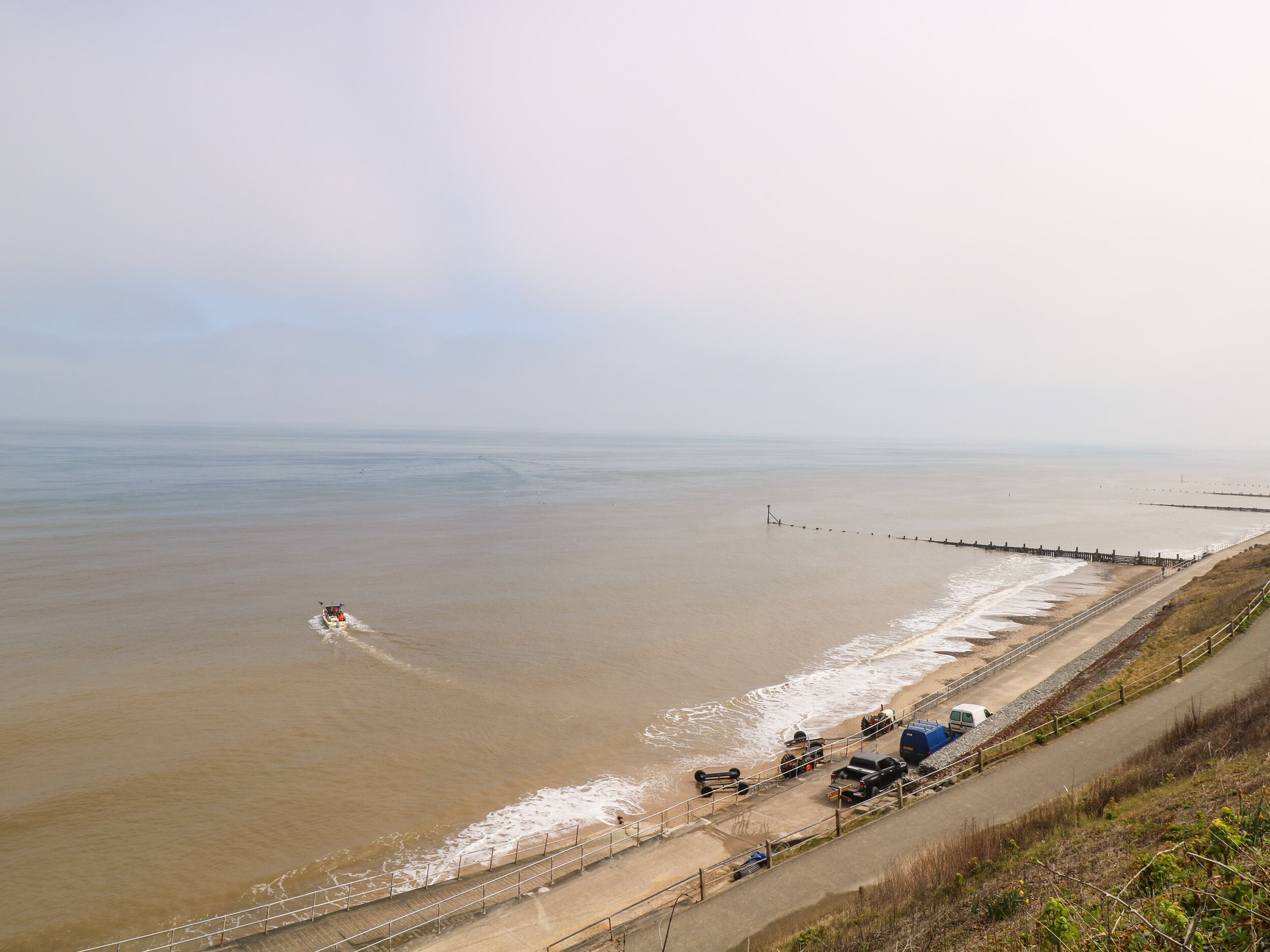 Une route côtière avec une plage sur la droite, un véhicule et un bateau sur l’eau.