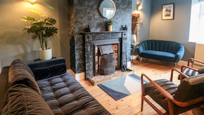 A modern living room with a fireplace, a blue sofa, a black armchair, and a potted plant.