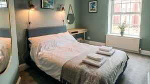 A bedroom with a bed, bedside lamps, a desk, and a window with a view of a building.