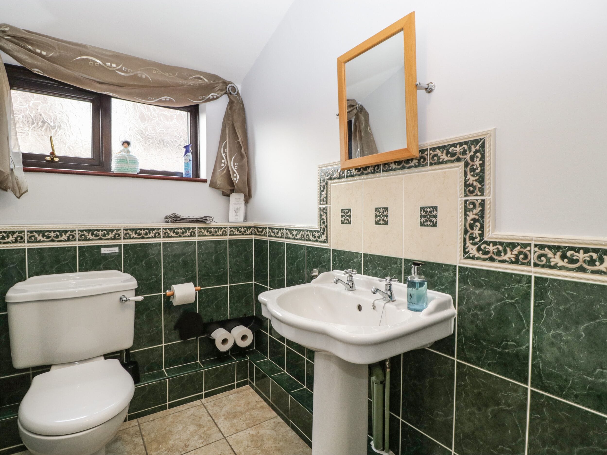 Een badkamer met toilet, wastafel en raam met gordijnen.