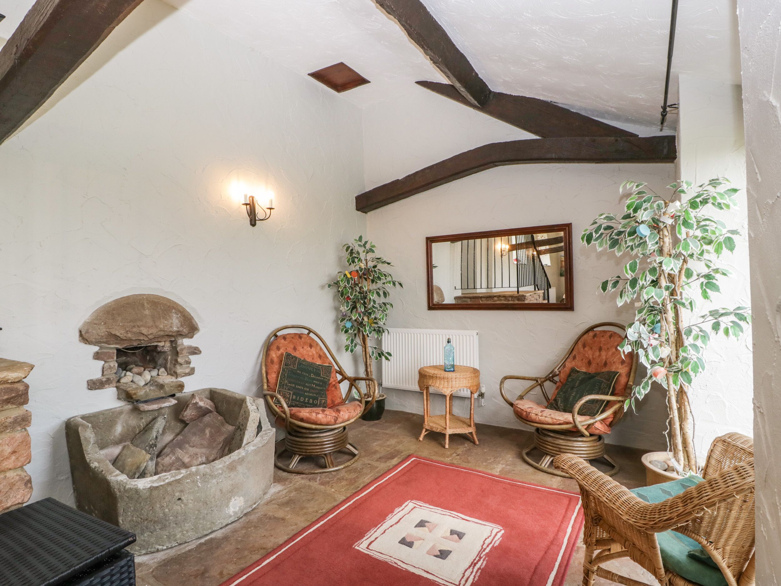 A rustic room with a stone fireplace, wicker chairs, a red rug, and a mirror on the wall.