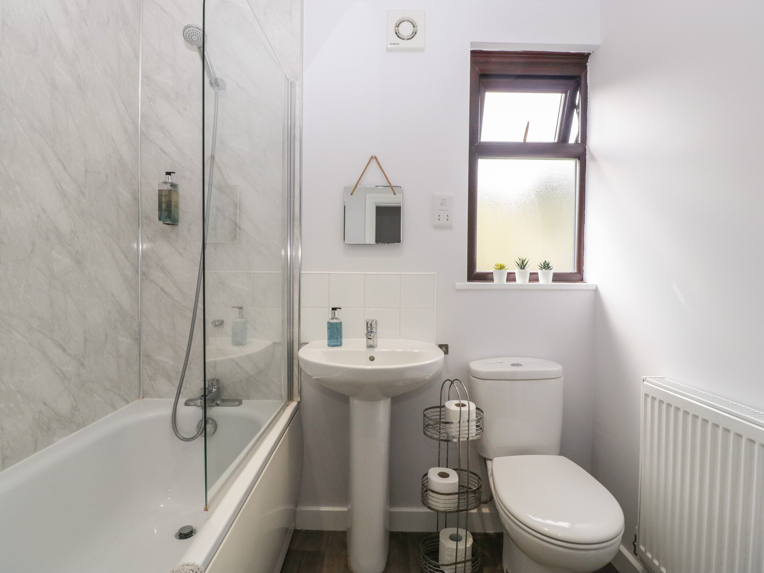Ein Badezimmer mit Badewanne, Waschtisch, Toilette und einem Fenster mit Pflanzen.